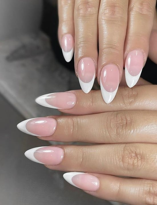 A closeup of a woman's fingernails with a pale pink nail polish base that has solid white tips