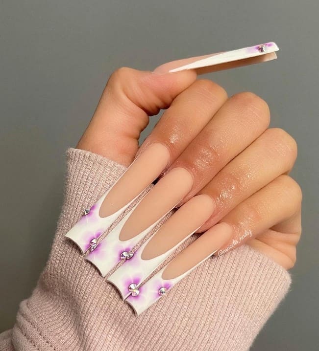 A closeup of a woman's fingernails with a nude matte nail polish that has purple polish to classic white French tips and silver studs