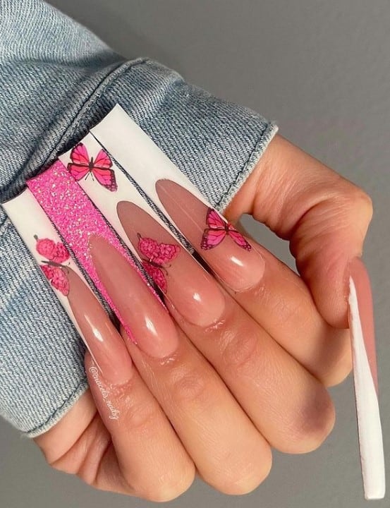 A closeup of a woman's fingernails with nude nail polish that has glittery pink nail polish on the accent nail, butterflies and white-tipped nails
