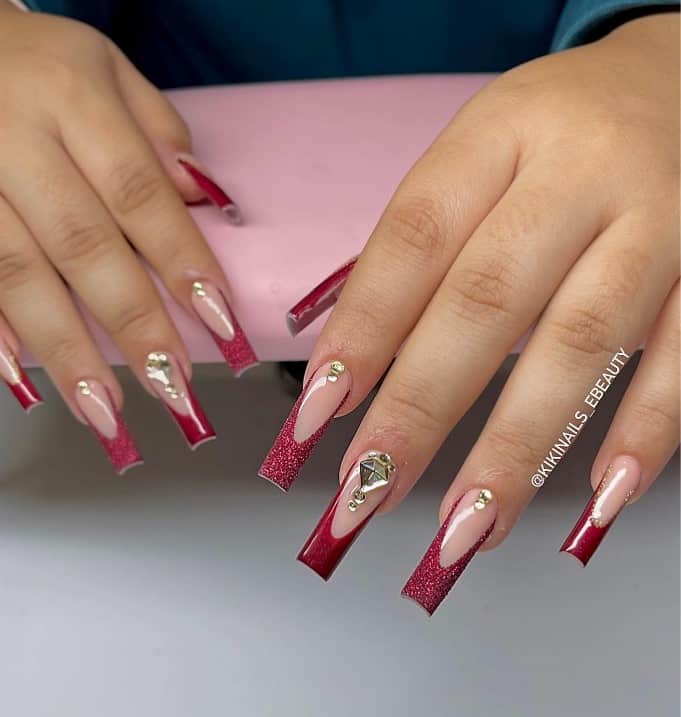 A woman's long acrylic fingernails with a nude nail polish that has white gems and glittery red tips