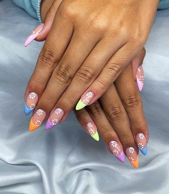 A closeup of a woman's fingernails with multicolored nail tips that has cute daisies on each nail