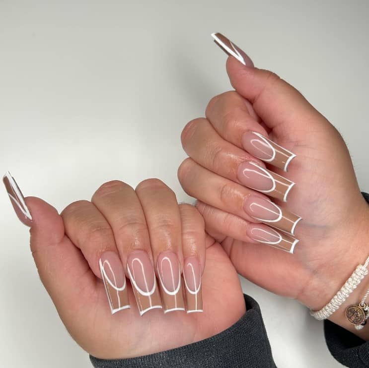 A woman's fingernails with a glossy nude colored nails that has brown tips with crisp white lines