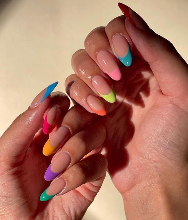 A closeup of a woman's fingernails with French tip color that has different shades of blue, pink, purple, orange, and green