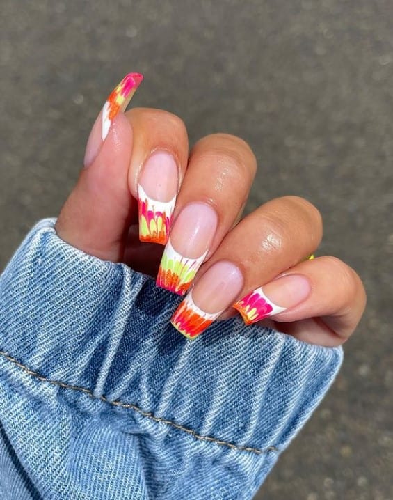 A woman's fingernails with a nude nail polish that has bright orange, pink, and yellow hues on nail tips 