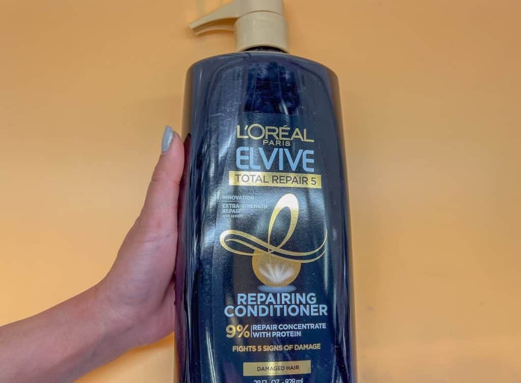 a woman's hand holding a bottle of L'oreal evive repairing conditioner