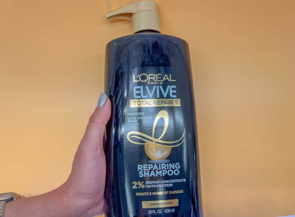 a woman's hand holding a bottle of L'oreal evive repairing shampoo.