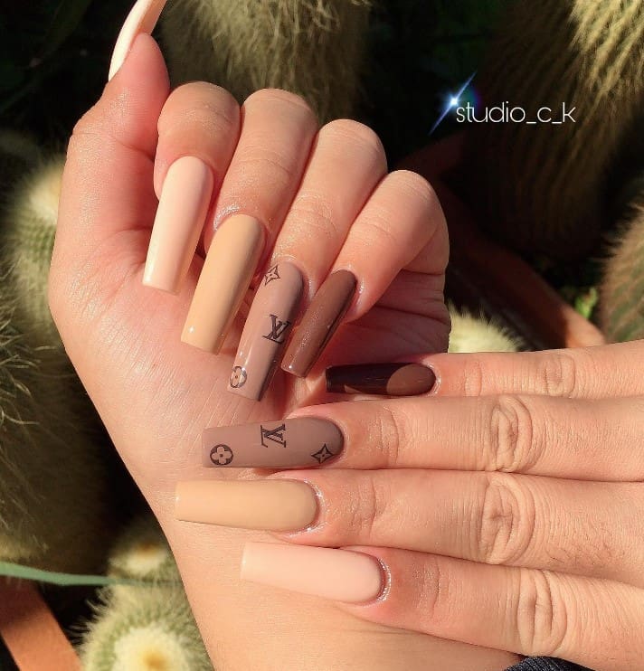 A closeup of a woman's fingernails with different shades of brown nail polish that has Louis Vuitton pattern on select nails