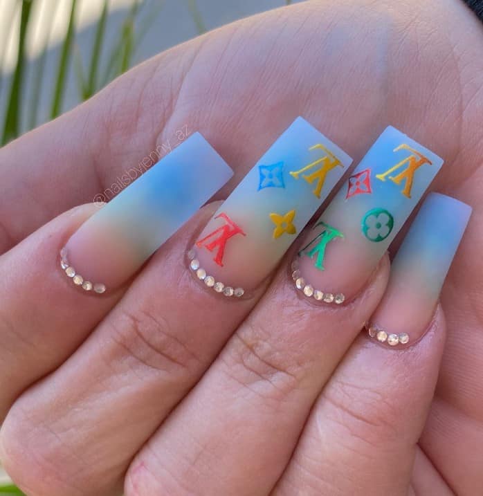 A closeup of a woman's fingernails with matte Pacific-blue nail polish that has bright multicolored Louis Vuitton patterns 
