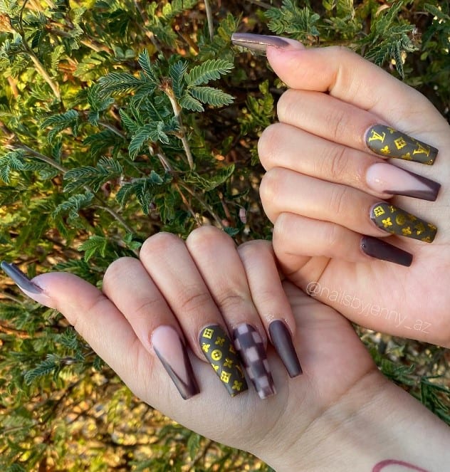A woman's fingernails with a mix of nude and decadent chocolate brown nail polish that has golden LV patterns