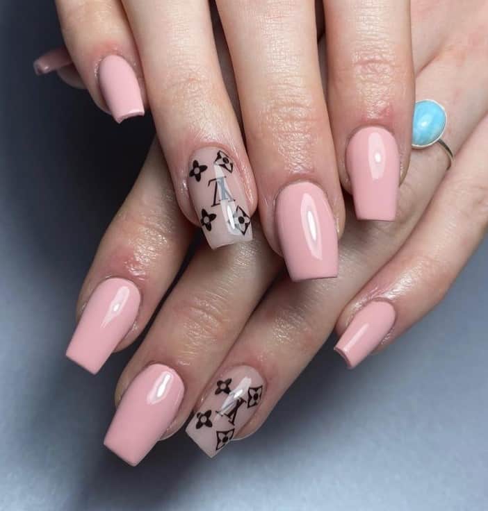 A closeup of a woman's fingernails with a glossy lemonade pink nail polish that has Louis V. nail art on select nails 