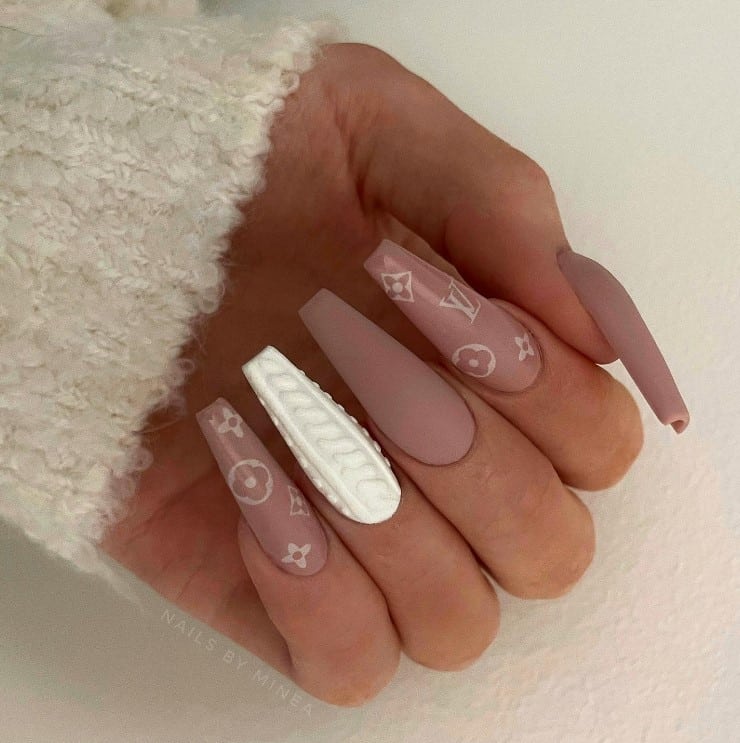 A closeup of a woman's fingernails with mocha nail polish that has white sweater pattern and LV patterns on select nails 