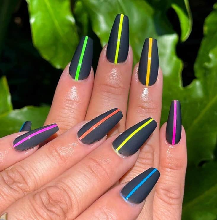 A closeup of a woman's long coffin fingernails with matte black nail polish base that has multicolored neon vibrant lines
