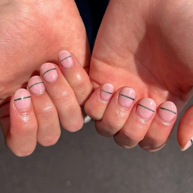 A closeup of a woman's fingernails with milky nude nails that has single horizontal green line in the middle of each nail