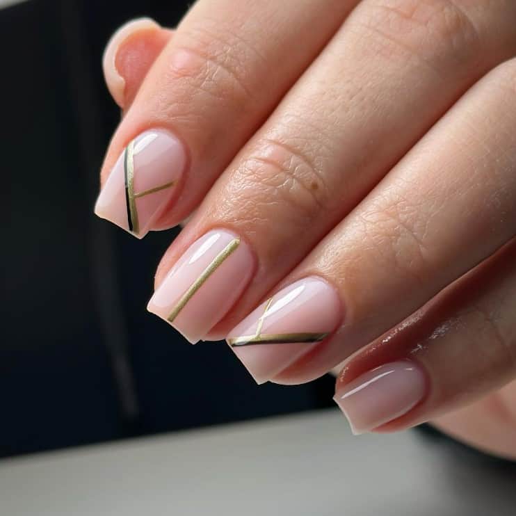 A closeup of a woman's fingernails with sheer pink base that has gold and black lines taking center stage