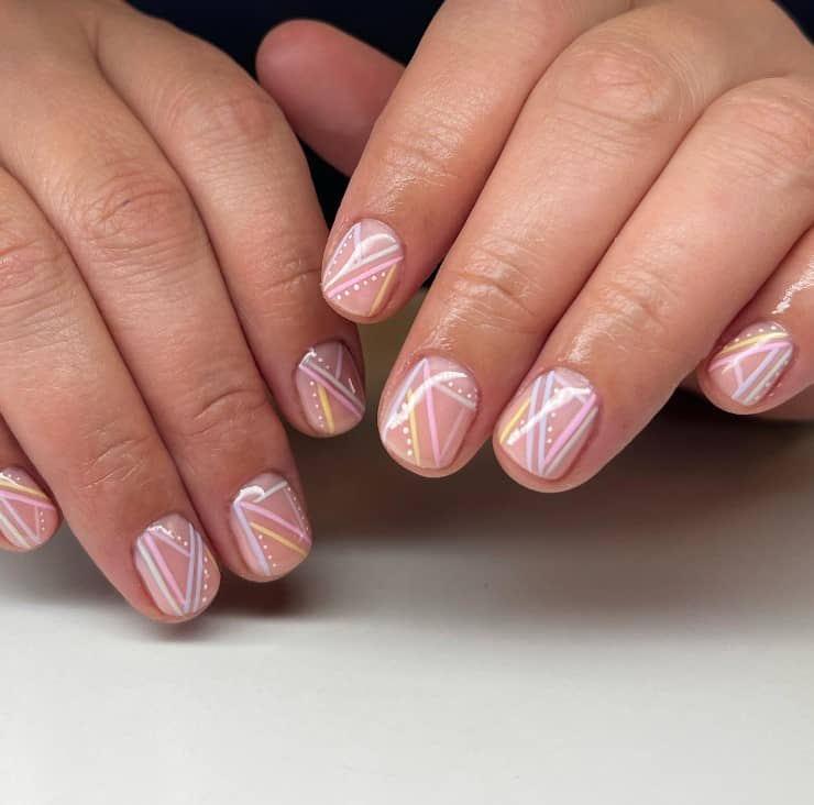 A closeup of a woman's fingernails with a pale pink nail polish that has pastel-colored lines and tiny white dots