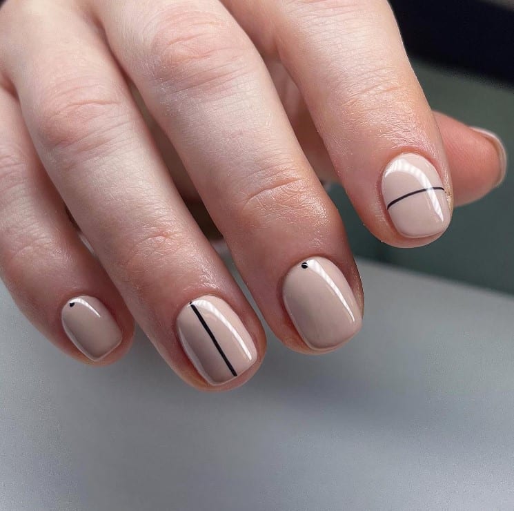 A closeup of a woman's fingernails with light beige nail polish that has alternating black dots and fine horizontal and vertical lines