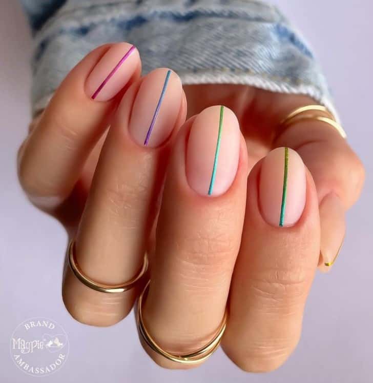 A closeup of a woman's fingernails with a matte peach base nail polish that has colorful nail art with line designs
