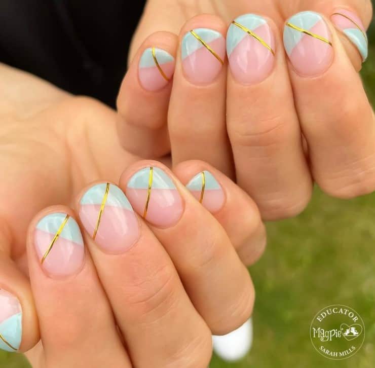 A closeup of a woman's fingernails with sheer pink shade that has pastel blue side French tips and diagonal gold lines