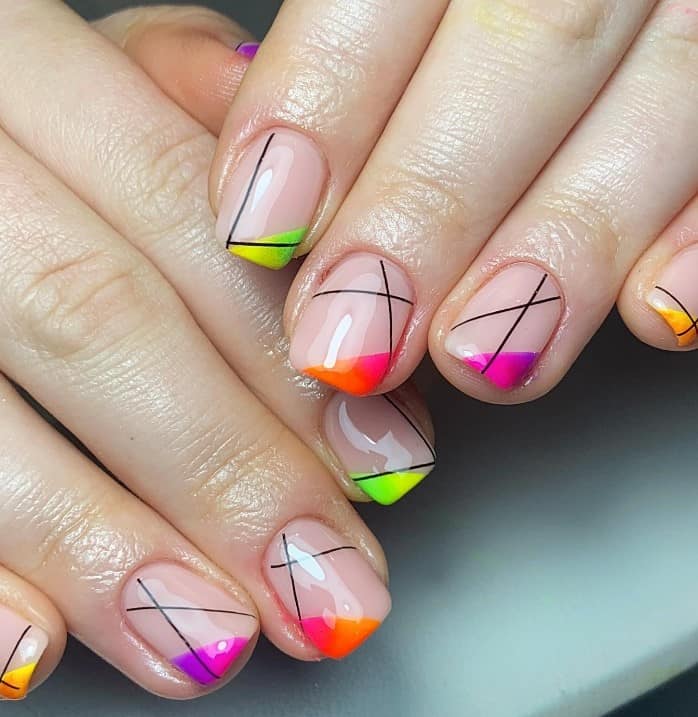 A closeup of a woman's fingernails with a glossy milky nude color that has black lines and multicolored neon ombré French tips