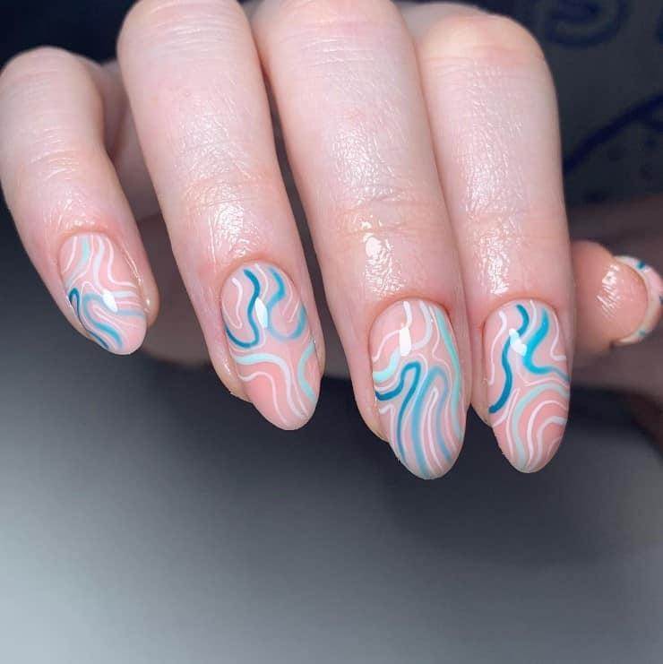 A closeup of a woman's fingernails with a peach nail polish base that has squiggly lines in different shades of blue and white