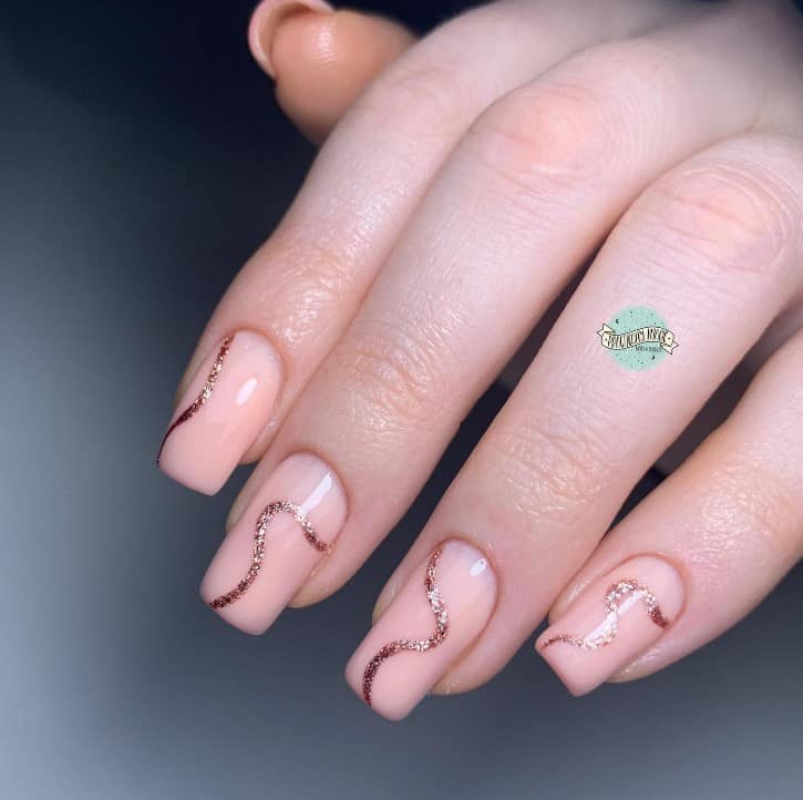 A closeup of a woman's fingernails with soft peach hue nails that has squiggly line in rose gold