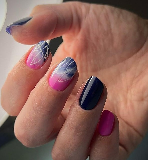 A closeup of a woman's fingernails with dark blue and pink nail polish alternately that has smudged and stained effect on the accent nails using white nail polish