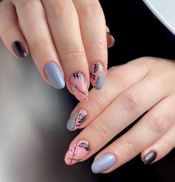 A closeup of a woman's fingernails with a combination of black, blue and black nail polish that has pastel blue side Frenchies, diagonal lines, leaves, tiny dots, and golden studs