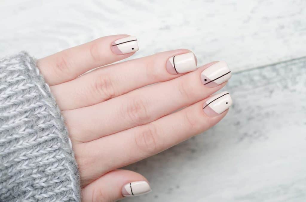 A woman's fingernails with a cream-colored nail polish that has black dots and asymmetrical lines