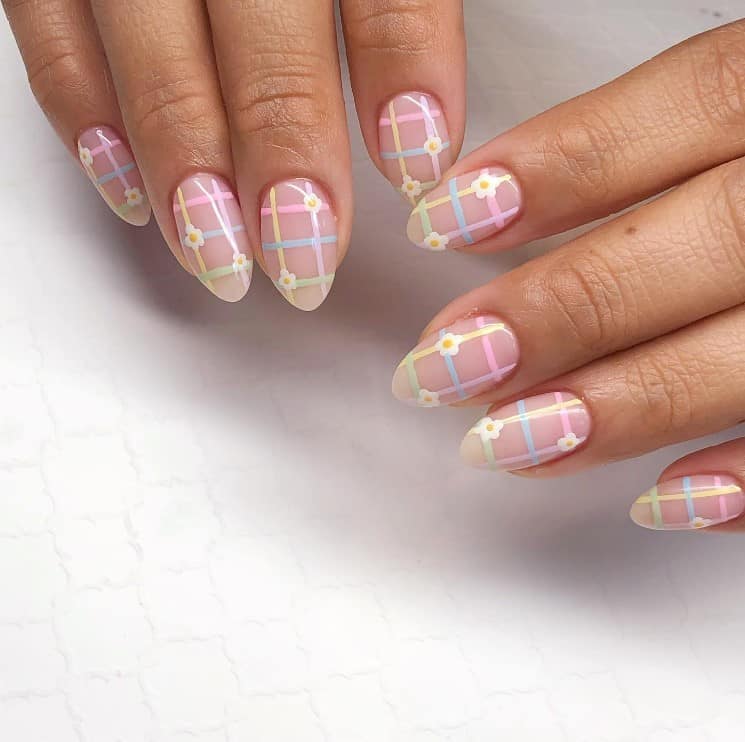 A closeup of a woman's fingernails with bare nails that has pastel-colored grid and two mini daisies