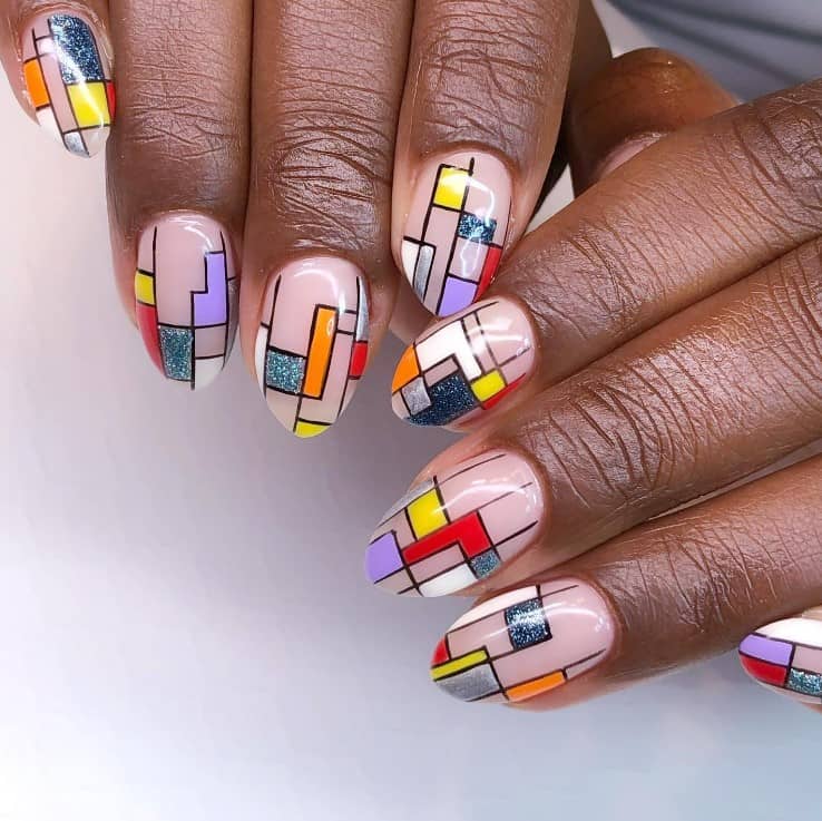 A closeup of a woman's fingernails with light nude nail polish base that has colorful Tetris-inspired shapes, lines and geometric patterns