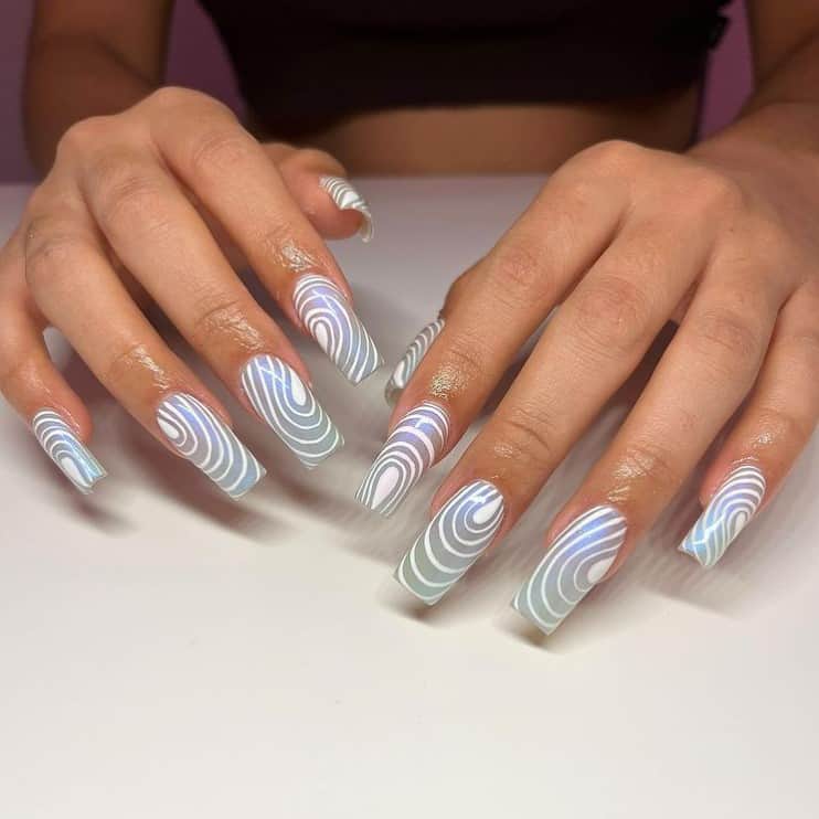 A woman's fingernails with sheer pale blue nail polish base that has white curvy lines
