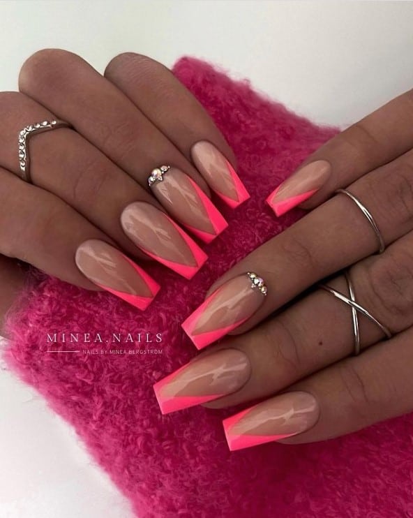A closeup of a woman's fingernails with nude nails that has neon pink deep V-cut tips and rhinestones