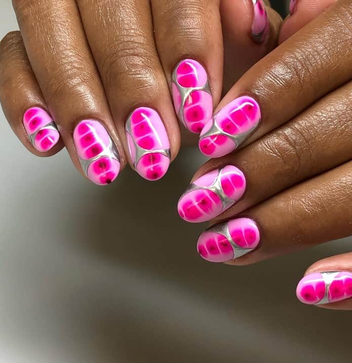 A closeup of a woman's fingernails with a light neon pink nail polish that has hot pink accents and “melted” silver scales