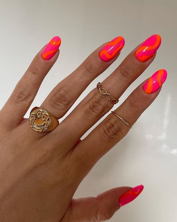 A woman's fingernails with a neon pink nails that has bright orange swirls