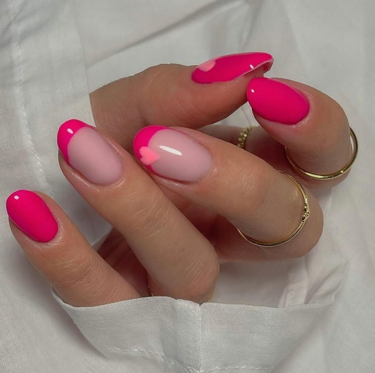 A closeup of a woman's fingernails with a combination of nude and hot pink nail polish base that has  pale pink hearts and neon pink French tips