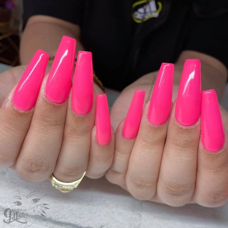 A closeup of a woman's long fingernails with a glossy neon pink nails 