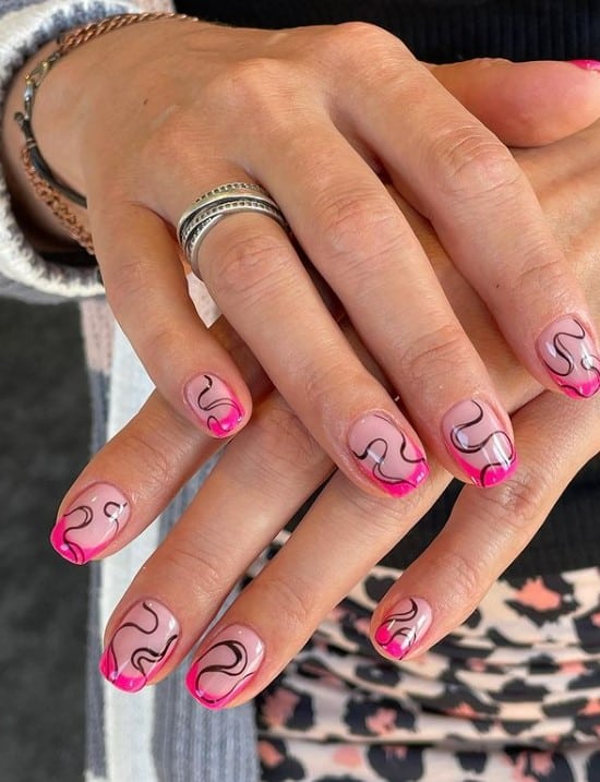 A closeup of a woman's fingernails with a nude nail polish base that has neon pink French tips and black swirls
