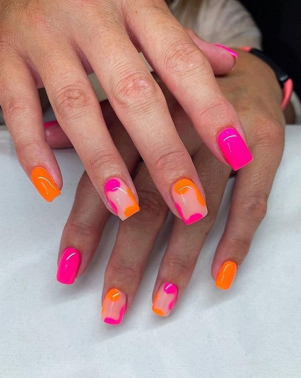 A closeup of a woman's fingernails with a nude, orange and neon pink nail polish that has abstract art nails in bold and bright colors