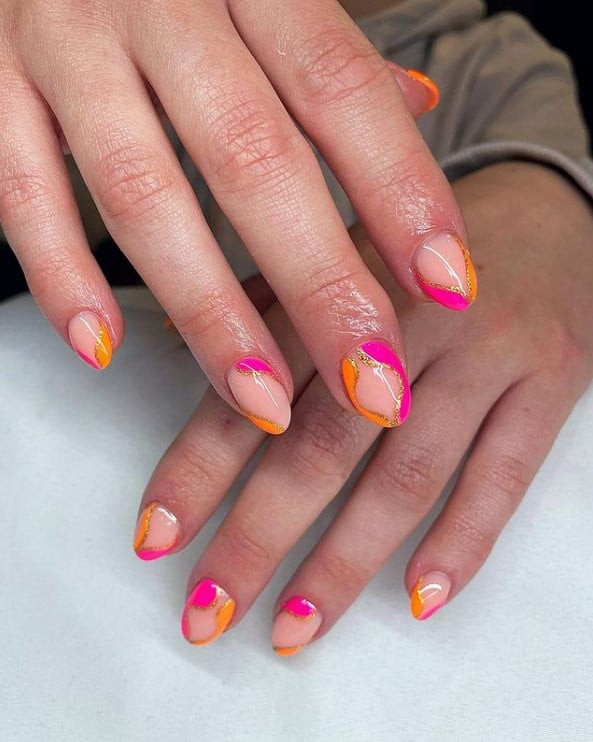 A woman's almond fingernails with a glossy nude nail polish that has neon pink and neon orange outlined with gold glitter
