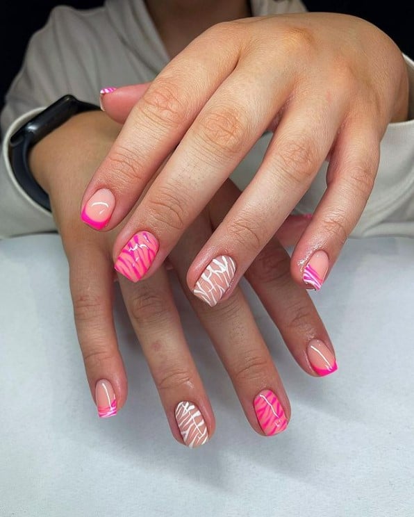 A closeup of a woman's fingernails with a nude and hot pink nail polish base that has white tiger striped nails with sold bold and tiger print French tips
