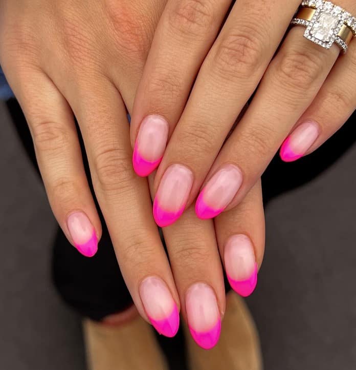 A closeup of a woman's fingernails with a glossy pale pink nail polish base that has neon pink tips
