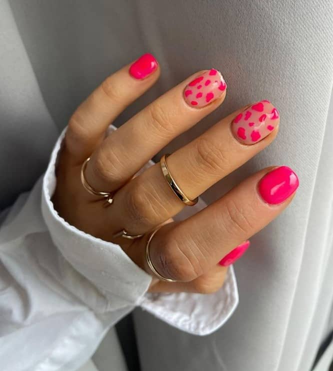 A closeup of a woman's fingernails with a combination of pale and hot pink polish that has neon pink cow print nail art