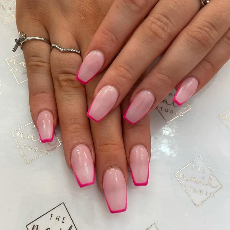 A closeup of a woman's fingernails with pale pink nail polish that has neon pink nail tips 