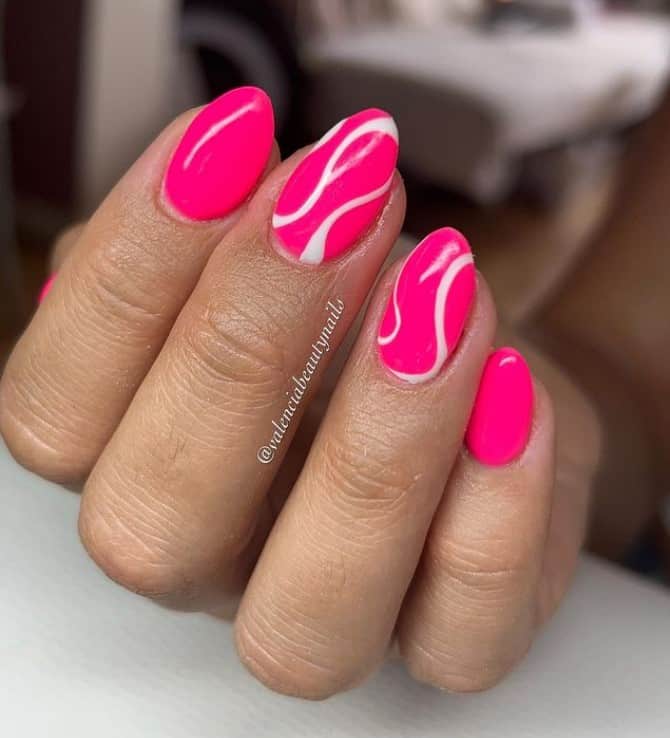 A closeup of a woman's fingernails with a neon pink nail polish base that has white swirls on select nails 