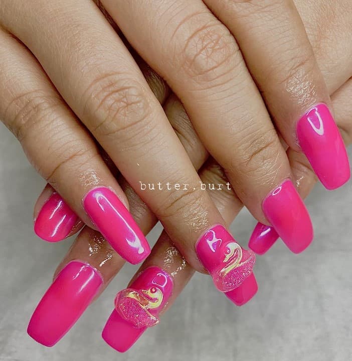 A closeup of a woman's fingernails with hot pink nail polish that has 3D nail art like translucent swans