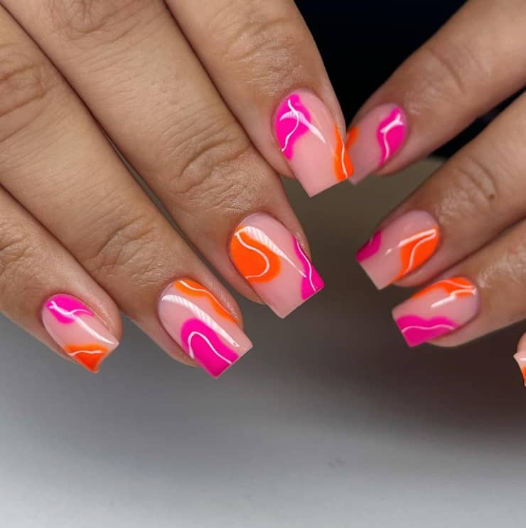 A closeup of a woman's fingernails with a nude pink nail base that has neon pink and neon orange corners with some streaks of white