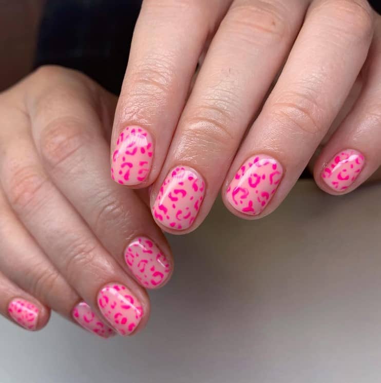 A closeup of a woman's fingernails with a light pink nail polish base that has hot pink cheetah print accents