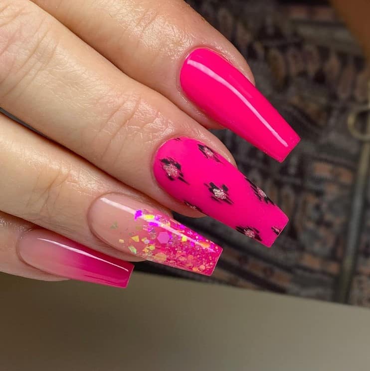 A closeup of a woman's fingernails with a neon pink nail polish that has cheetah print, chunky glitter, ombre