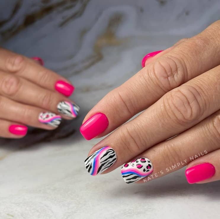 A closeup of a woman's fingernails with a neon pink and white nail polish that has zebra stripes and cheetah print accents