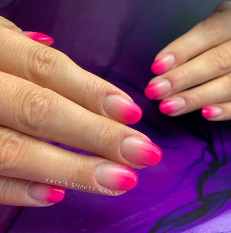 A closeup of a woman's fingernails with nude and hot pink ombre nail polish 